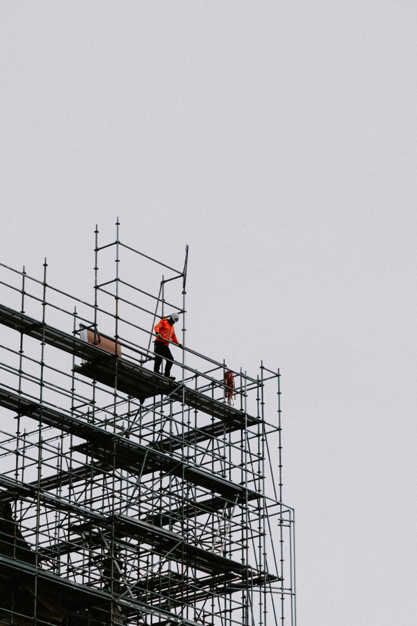 Gerüstbauer in oranger Warnkleidung auf einem hohen Arbeitsgerüst