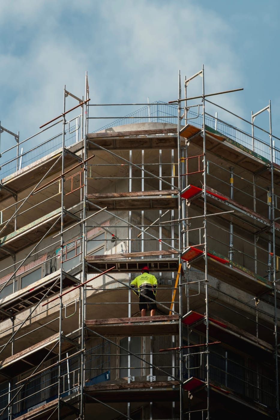 Vom Gerüstbauer gestelltes Eckgerüst an einem Neubau, ein Monteur arbeitet auf der oberen Lage