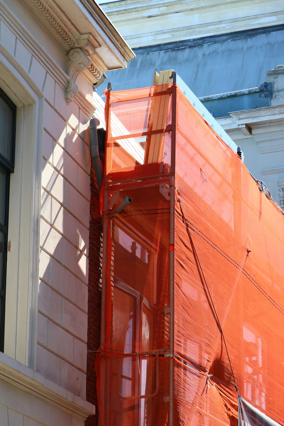 Vom Gerüstbauer mit orangefarbenem Schutznetz eingekleidetes Fassadengerüst an einem Altbau